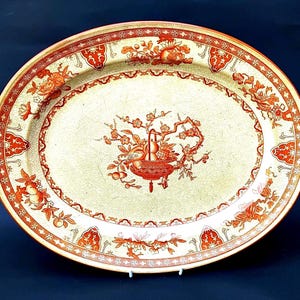 May include: An oval ceramic platter featuring a cream-colored base with a fine crackle glaze finish. The rim and center are decorated with intricate orange and red floral and fruit motifs, including blossoms and a central basket of fruit.