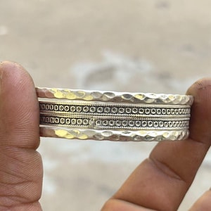 May include: A stack of silver rings with hammered and beaded textures. The rings are held in a hand, showcasing the intricate details of the jewellery. The rings have a vintage or artisan style.