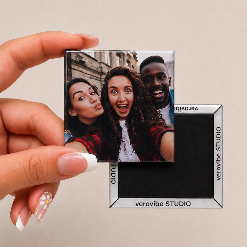 K&ouml;nnte beinhalten: Ein quadratischer K&uuml;hlschrankmagnet mit einem Farbfoto von drei Personen, die l&auml;cheln und f&uuml;r ein Selfie posieren. Die R&uuml;ckseite des Magnets ist schwarz mit einem silbernen Rand, der an allen vier Seiten mit verovibe STUDIO bedruckt ist.
