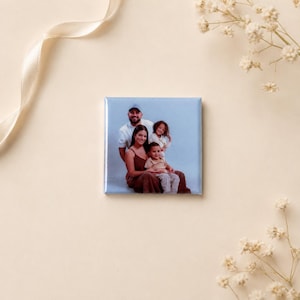 K&ouml;nnte beinhalten: Ein quadratischer Magnet mit einem aufgedruckten Foto einer vierk&ouml;pfigen Familie. Das Bild zeigt einen Mann, eine Frau und zwei Kinder, die gemeinsam vor einem hellblauen Hintergrund posieren. Der Magnet hat eine gl&auml;nzende Oberfl&auml;che.