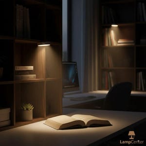 May include: A well-lit workspace featuring an open book on a desk, illuminated by a small, round LED light. Bookshelves and a computer are visible in the background. The scene is bathed in warm light, creating a cozy reading environment.