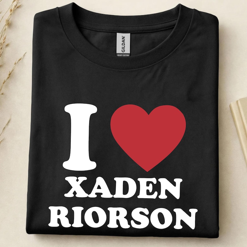 May include: Black t-shirt with the text "I ❤️ XADEN RIORSON" in white, with a red heart symbol. The shirt is folded neatly, showcasing the design prominently. The brand tag "GILDAN" is visible.