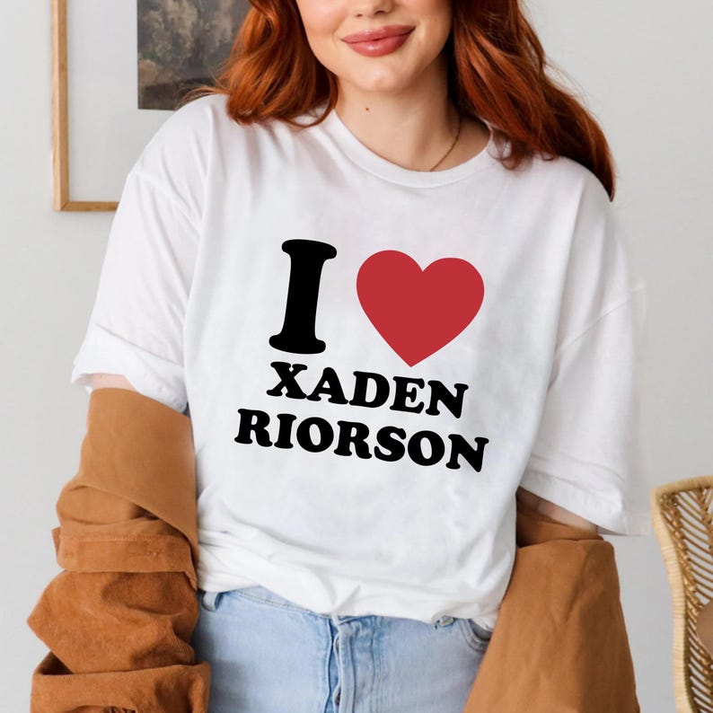 May include: White t-shirt with the text "I &hearts; XADEN RIORSON" in black and red. The "I" is black, the heart is red, and the names are in a bold, sans-serif font. The shirt is a casual, everyday wear item.