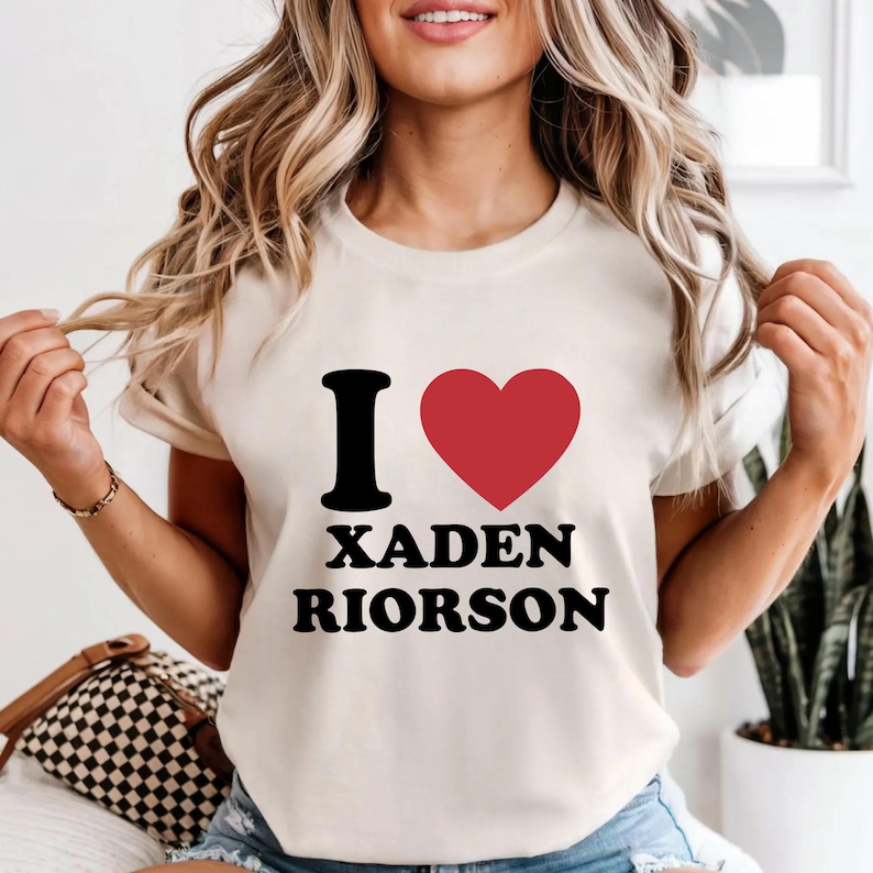 May include: Cream-colored t-shirt with the text "I ❤️ XADEN RIORSON" in black and red. The design features a black letter "I" followed by a red heart and the names in a bold font. The shirt has short sleeves.