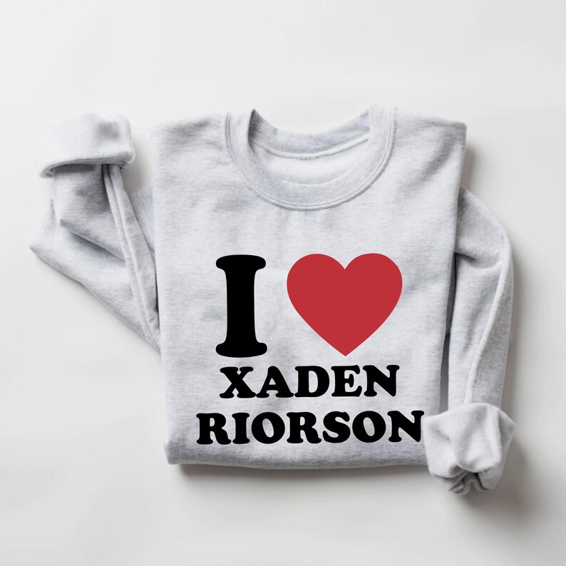 May include: A light gray sweatshirt with the text "I &hearts; XADEN RIORSON" in black and a red heart. The sweatshirt is folded, with the sleeves cuffed.