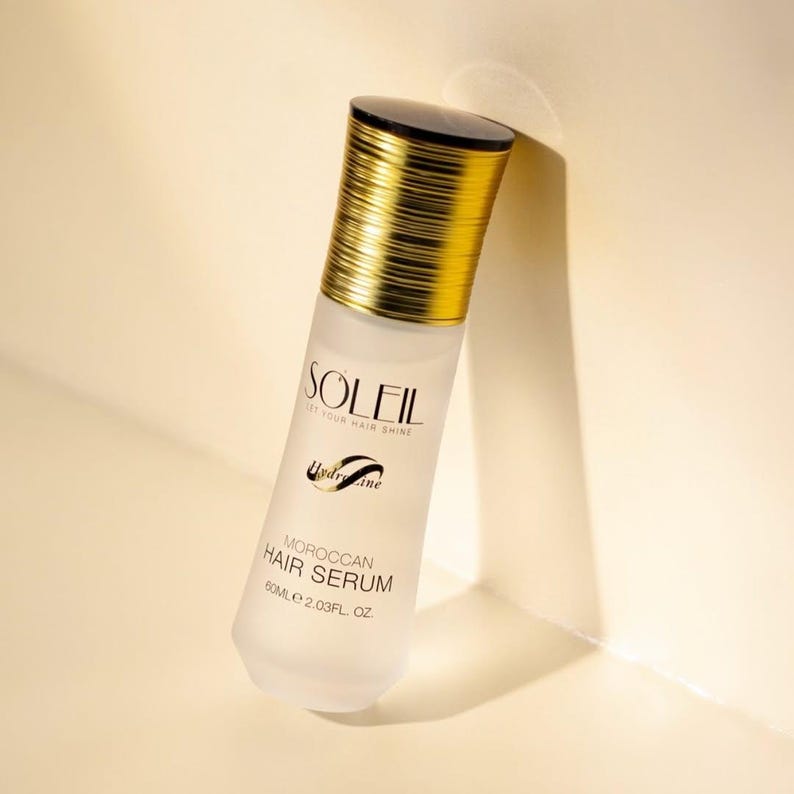 May include: A frosted glass bottle of Moroccan hair serum with a gold cap and black top. The bottle is labeled "SOLEIL" and "HydraLine", with the text "Moroccan Hair Serum" and "60ml 2.03 fl. oz."