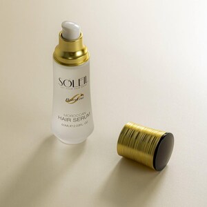 May include: A white and gold Moroccan Hair Serum bottle with the text "SOLEIL" and "Moroccan Hair Serum". The bottle is next to its gold and black cap. The bottle contains 2.03 fl oz of serum.