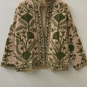 以下が含まれることがあります： ベージュのジャケット、オリーブグリーンの花の刺繍入り。 ジャケットはスタンドカラーと長袖です。 内側の裏地はストライプ柄です。 右下には「belafabexport」の文字が見えます。