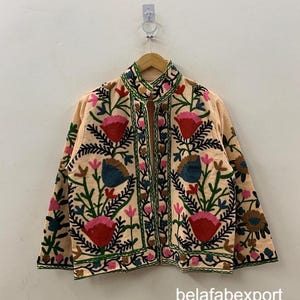 Puede incluir: Chaqueta bordada de color melocotón con cuello alto y diseño floral. La chaqueta presenta bordados florales rojos, rosas, azules y verdes. El texto "belafabexport" es visible en la parte inferior derecha de la chaqueta.