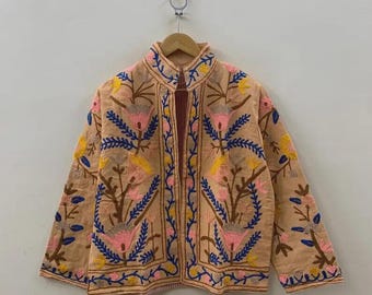 May include: A peach-colored jacket with intricate floral embroidery in pink, blue, yellow, and brown. The jacket features a high collar and is hanging on a wooden hanger. The text "belafabexport" is visible at the bottom right.