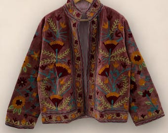 May include: A maroon velvet jacket with intricate floral embroidery in shades of orange, yellow, teal, and green. The jacket features a high collar and a striped lining. The embroidery is concentrated along the edges and sleeves.