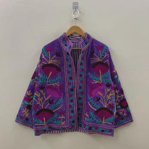 May include: A purple embroidered jacket with a mandarin collar. The jacket features a floral design in shades of pink, teal, and gold. The text "belafabexport" is visible at the bottom of the image.