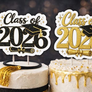 Könnte beinhalten: Zwei Tortenaufsätze zur Graduierung mit dem Text "Class of 2026". Einer ist schwarz und gold, der andere ist goldfarben. Jeder Aufsatz enthält eine Abschlusskappe und ein Diplom. Die Kuchen sind weiß mit goldenen Akzenten.