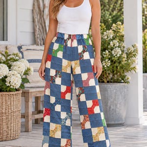 May include: Wide-leg trousers featuring a patchwork quilt design with a repeating pattern of blue, cream, red, green, and floral fabric squares. The pants have an elasticized waistband and a loose, straight-leg fit that reaches the ankles.