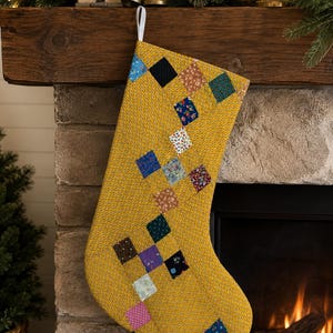 May include: A mustard yellow Christmas stocking featuring a quilted patchwork design with small, multi-colored floral and geometric fabric squares arranged in a diagonal pattern across the front, finished with a white hanging loop at the top.