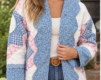 May include: A quilted jacket featuring a patchwork design with blue floral, pink floral, and blue plaid fabric squares. The jacket has a scalloped front edge, long sleeves, and a white base layer underneath, paired with blue denim jeans and a brown belt.