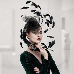 Könnte beinhalten: Ein schwarzer Fascinator-Kopfschmuck mit einer strukturierten Tüllblume und einer Anordnung aus dünnen, geschwungenen Drahtstielen, die mit schwarzen Federn verziert sind. Der Kopfschmuck wird seitlich getragen und erzeugt eine geschwungene Silhouette.