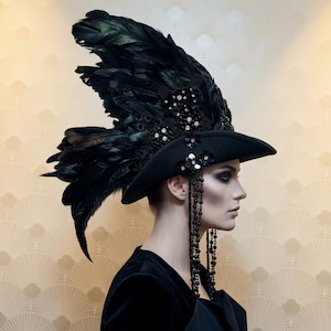 Può includere: Cappello nero con ampia tesa e dettagli elaborati di piume. Il cappello è adornato con perline e paillettes nere, e lunghe file di perline pendenti. Un accessorio di costume in stile gotico o teatrale.