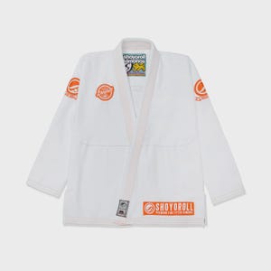 Puede incluir: Kimono de Jiu-Jitsu blanco con detalles en naranja. El kimono muestra el nombre de la marca "SHOYOROLL" en naranja en el pecho, las mangas y la parte inferior. Tiene cuello en V y cinturón blanco. Fabricado con material resistente.