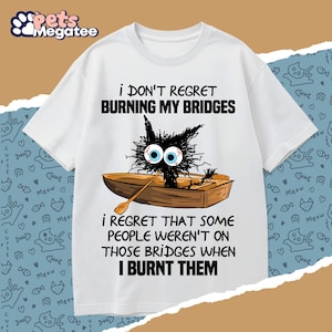 May include: White t-shirt with a humorous graphic of a black cat in a boat, rowing with wide eyes. Text reads "I DON'T REGRET BURNING MY BRIDGES" and "I REGRET THAT SOME PEOPLE WEREN'T ON THOSE BRIDGES WHEN I BURNT THEM."