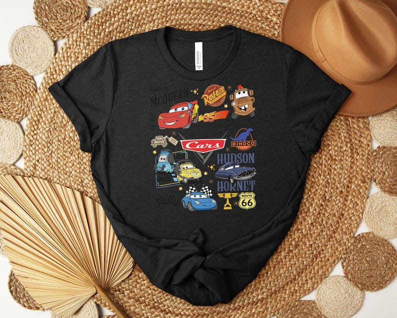 Puede incluir: Camiseta negra con un gr&aacute;fico colorido que muestra personajes y logotipos de la pel&iacute;cula "Cars". El dise&ntilde;o incluye a Rayo McQueen, Mate y otros personajes, junto con el logotipo de "Cars" y la se&ntilde;alizaci&oacute;n de la Ruta 66.