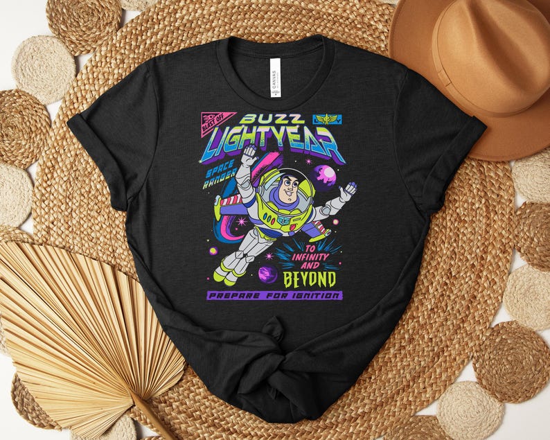May include: Black t-shirt featuring a colorful graphic of Buzz Lightyear in a space scene. The design includes the words "Buzz Lightyear", "Space Ranger", and "To Infinity and Beyond". The shirt is a crew neck.