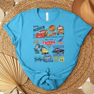 Puede incluir: Una camiseta turquesa con un gr&aacute;fico colorido de personajes de la pel&iacute;cula Cars de Disney Pixar. El dise&ntilde;o incluye a Rayo McQueen, Mate, Sally y otros personajes, junto con el texto "Cars".