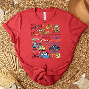 Puede incluir: Camiseta roja con un gr&aacute;fico colorido de personajes de la pel&iacute;cula Cars de Disney Pixar. El dise&ntilde;o incluye a Rayo McQueen, Mate, Sally y otros personajes, junto con el texto "Cars" y "Route 66".