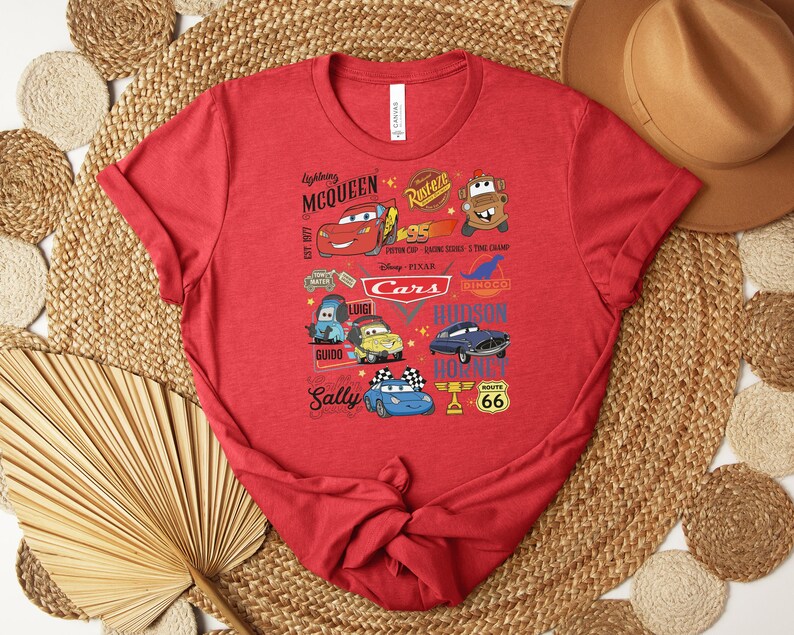 Puede incluir: Camiseta roja con un gr&aacute;fico colorido de personajes de la pel&iacute;cula Cars de Disney Pixar. El dise&ntilde;o incluye a Rayo McQueen, Mate, Sally y otros personajes, junto con el texto "Cars" y "Route 66".