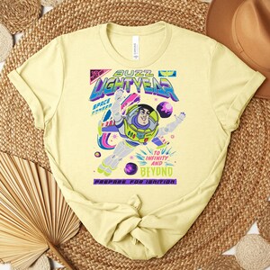 May include: A light yellow t-shirt featuring a graphic of Buzz Lightyear from Toy Story. The design includes the words "Buzz Lightyear" in a colorful font, with the phrase "To Infinity and Beyond." The shirt is made of soft material.