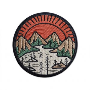 May include: Embroidered patch featuring a scenic mountain landscape with a setting sun. The design includes brown mountains, green trees, a river, and a campsite, all set against a vibrant orange sky. The patch is circular with a black border.
