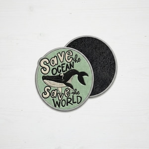 May include: Round patch with a light green background and a black and white whale illustration. The patch has the text "Save the Ocean Save the World" in white lettering. The patch is on a white surface.