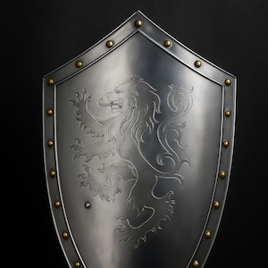 May include: A silver-colored shield with a lion crest design. The shield has a pointed bottom and is edged with brass-colored rivets. The lion is in a heraldic pose, with its front paws raised.
