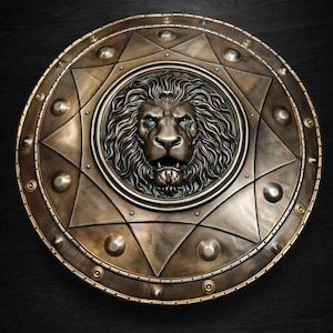 May include: A bronze-colored shield with a detailed lion's head at the center. The shield features a circular design with star and geometric patterns, and is accented with rivets. The overall aesthetic is reminiscent of ancient armor.