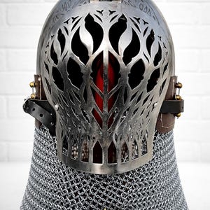 May include: A silver-colored medieval helmet with intricate cut-out designs on the face guard. The helmet features a hinged top and is set over a chainmail coif. The word "LEGENDARY" is printed at the bottom.