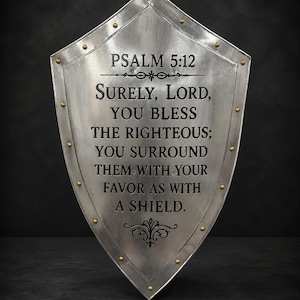 May include: A silver-colored metal shield with a pointed bottom and a reinforced border featuring small brass-colored rivets. The center is engraved with the text Psalm 5:12, Surely, Lord, you bless the righteous; you surround them with your favor as with a shield.