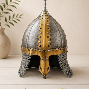 May include: A steel helmet with a textured grey finish, featuring a pointed top spike and gold-colored metal trim with scalloped edges and rivets. A chainmail aventail hangs from the base, and the word LEGENDARY is printed below the helmet.
