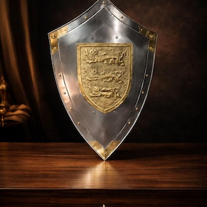 May include: A silver and gold shield with a gold emblem in the centre. The shield has a polished metal finish with gold accents on the corners and emblem. The word "LEGENDARY" is at the bottom.