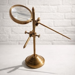 May include: A brass-toned magnifying glass on a stand, with a round lens and adjustable arms. The base is circular, and the text "LEGENDARY" is at the bottom. The background is a white brick wall.
