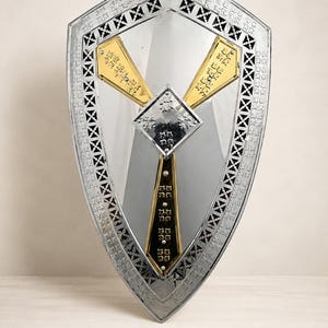 May include: A silver-toned shield with a reflective surface, featuring a decorative border with cut-out patterns. The centre displays a diamond-shaped silver plate and three gold-coloured accents. The word LEGENDARY is printed at the bottom.