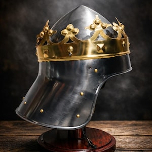 May include: A medieval-style helmet with a gold crown detail. The helmet is made of silver metal and is mounted on a wooden stand. The crown features ornate gold accents. The background is dark and smoky.