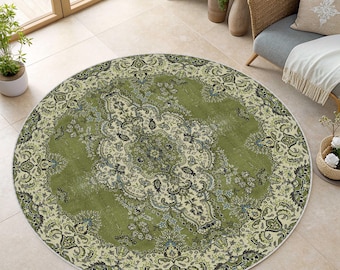 May include: A round, olive green rug with an intricate floral pattern. The rug has a cream-colored border with a detailed design. The rug is placed on a tiled floor, with a chair and plants in the background.