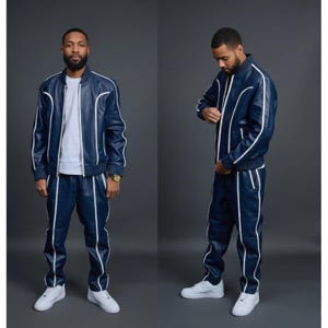 May include: A navy blue tracksuit with white piping. The jacket is a bomber style with a zipper closure. The pants have an elastic waistband. The outfit is paired with white sneakers. The tracksuit is made of a leather-like material.