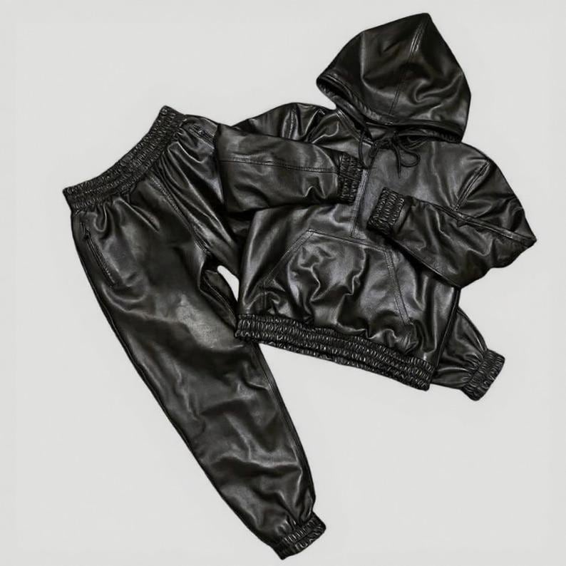 Puede incluir: Un conjunto de ch&aacute;ndal de cuero negro, que incluye una sudadera con capucha y pantalones a juego. La sudadera tiene un bolsillo delantero y una capucha con cord&oacute;n. Los pantalones tienen cintura y pu&ntilde;os el&aacute;sticos. El conjunto es de polipiel brillante.