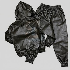 Puede incluir: Un conjunto negro de imitaci&oacute;n de cuero que incluye una chaqueta con capucha y pantalones a juego. La chaqueta tiene cierre de cremallera y pu&ntilde;os y cintura el&aacute;sticos. Los pantalones tienen cintura y pu&ntilde;os el&aacute;sticos. El conjunto est&aacute; hecho de material de cuero sint&eacute;tico brillante.