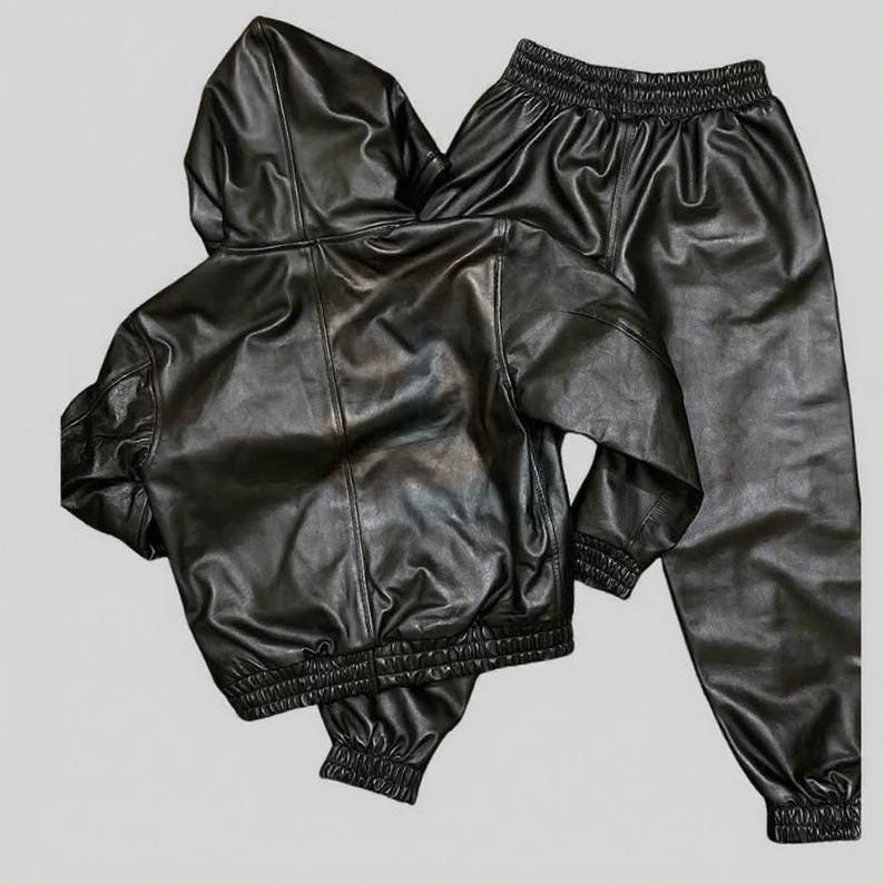 Puede incluir: Un conjunto negro de imitaci&oacute;n de cuero que incluye una chaqueta con capucha y pantalones a juego. La chaqueta tiene cierre de cremallera y pu&ntilde;os y cintura el&aacute;sticos. Los pantalones tienen cintura y pu&ntilde;os el&aacute;sticos. El conjunto est&aacute; hecho de material de cuero sint&eacute;tico brillante.