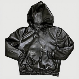 Puede incluir: Sudadera con capucha de cuero negro con capucha con cord&oacute;n, bolsillo tipo canguro y pu&ntilde;os y dobladillo acanalados. La sudadera con capucha es de color negro liso y tiene una textura suave y brillante. Es una prenda de abrigo informal.