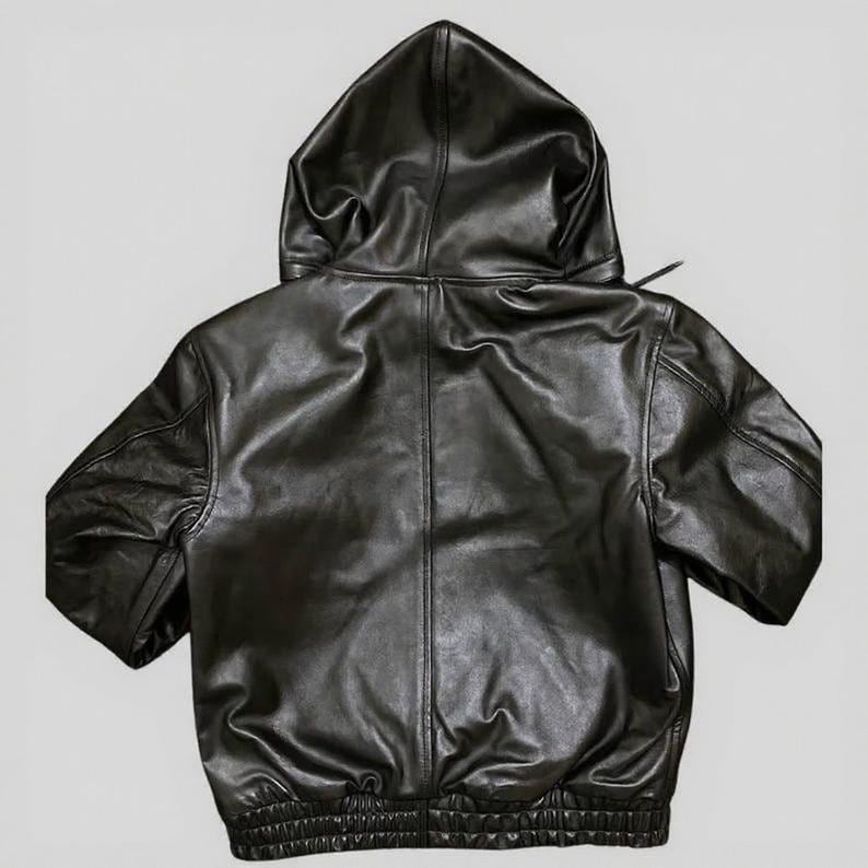 Puede incluir: Chaqueta con capucha de cuero negro con mangas cortas. La chaqueta presenta una capucha con cord&oacute;n, un dobladillo acanalado y un dise&ntilde;o cl&aacute;sico de chaqueta bomber. El cuero tiene un aspecto ligeramente texturizado.