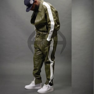 May include: Olive green leather jacket and matching pants with white side stripes. The jacket has a collared neckline and button closure. The pants have an elastic waistband. The outfit is paired with white sneakers.