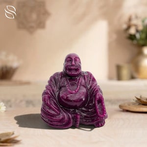 Può includere: Statua di Buddha seduto scolpita in una pietra preziosa viola scuro. La figura ha un'espressione serena ed è adornata da una collana. La statua è un oggetto decorativo, probabilmente per l'arredamento della casa o la pratica spirituale.
